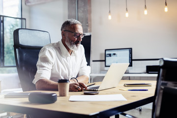 Adult professional businessman wearing a classic glasses and working at the wood table in modern...