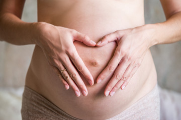 Fototapeta na wymiar Pregnant woman holding hands in a heart shape on her baby bump