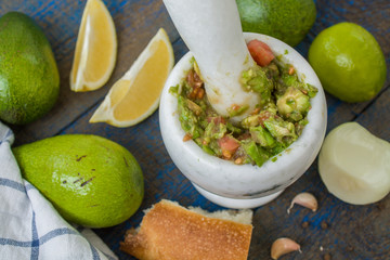 Guacamole - latin american sauce and ingredients (avocado, tomatoes, onion, lemon, garlic, lime) onblue wooden background. Love for a healthy raw food concept.  Top view