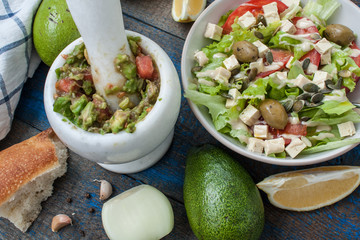 Guacamole - latin american sauce and ingredients (avocado, tomatoes, onion, lemon, garlic, lime) and green salad with tofuonblue wooden background. Love for a healthy raw food concept.