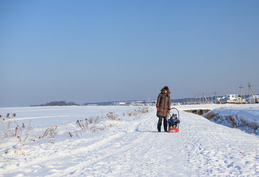 Mother and her little son with sled walking on cold winter day 
