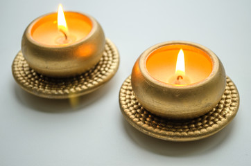 Obraz na płótnie Canvas Two burning decorative candles in gold color on a light background