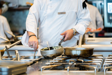 Chef heating saucepan on stove with coworker in background
