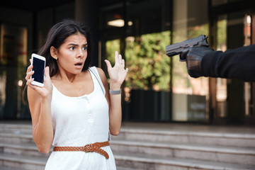 Scared woman holding cell phone threatened by criminal with gun