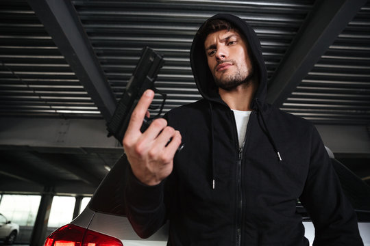 Serious young criminal man in hoodie holding gun