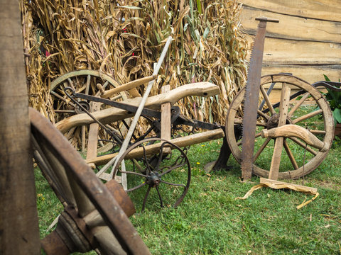 Picture of the old cart-wheels at the farm. Wooden and iron cart-wheels with saw on green grass. Agricultural implement before wooden fence and haulm.
