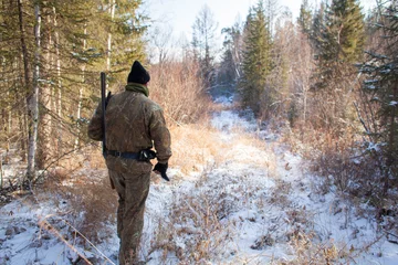 Foto op Plexiglas a hunter in the winter woods with a gun in camouflage clothing. © nikstar_2012
