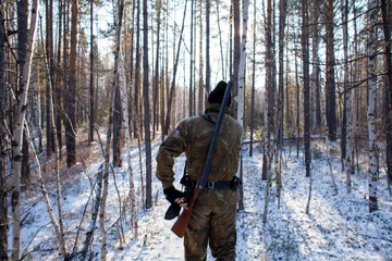 Poster a hunter in the winter woods with a gun in camouflage clothing. © nikstar_2012