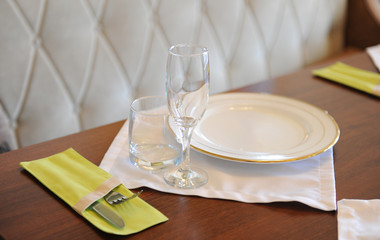 Served table in restaurant. White plates, glasses on a white cloth on wooden surface