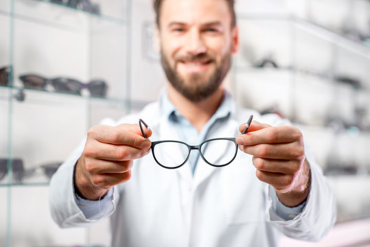 Handsome ophthalmologist holding eyeglasses for a try out. Optometrist offering to wear a pair of glasses. Image with small deph of field focused on the hands and glasses