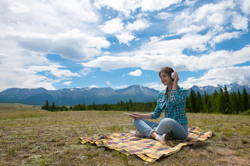 Fototapeta na wymiar Woman in headphones listening music in a field and at the mountain.