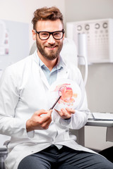 Portrait of handsome ophthalmologist with eye model in front of the eye chart in the cabinet