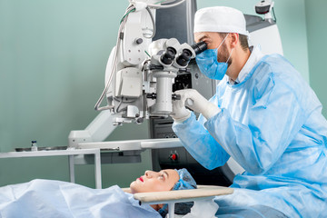 Surgeon looking into the microscope at the eye of female patient at the operating room