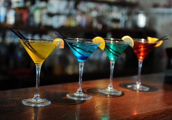 Four colored cocktails on the bar. Yellow, blue, green, red. Decorated with a lemon slice