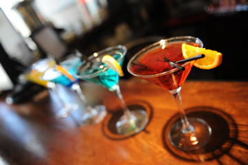 Four colored cocktails on the bar. Yellow, blue, green, red. Decorated with a lemon slice