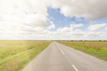 Asphalt road through the field with green grass under blue sky with clouds