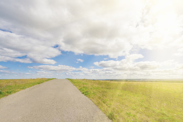 Asphalt road through the field with green grass under blue sky with clouds