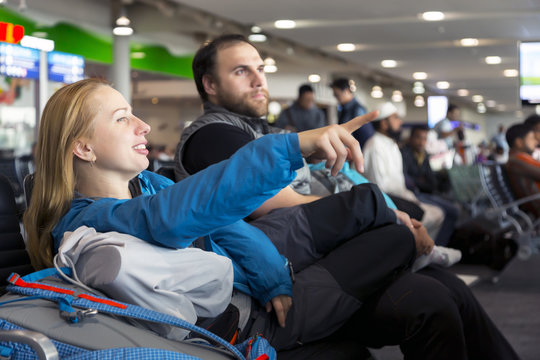 Man and woman sitting at airport terminal and pointing