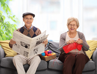 Mature man holding a newspaper and a mature woman knitting sitti