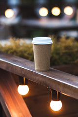 Cup takeaway coffee on cafe veranda with bokeh lights
