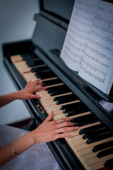 Woman's hands on the piano keyboard with notes.