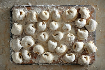 The process of preparation of Russian meat dumplings. Homemade raw dumplings with flour on a wooden board. View from above.