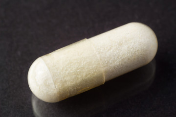 Glucosamine capsule, food supplement pills on glossy dark background, macro image.