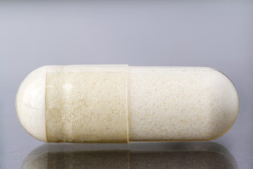 Glucosamine capsule, food supplement pills on glossy dark background, macro image.