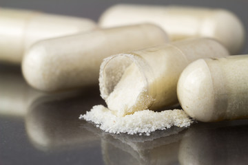 Cut glucosamine capsules, food supplement pills on glossy dark background, macro image.