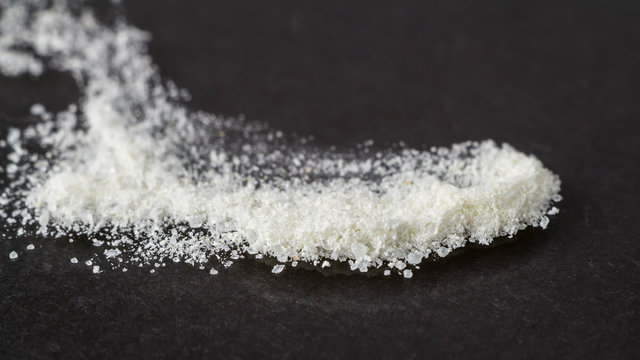 White glucosamine crystals powder supplement on glossy dark background, macro image.