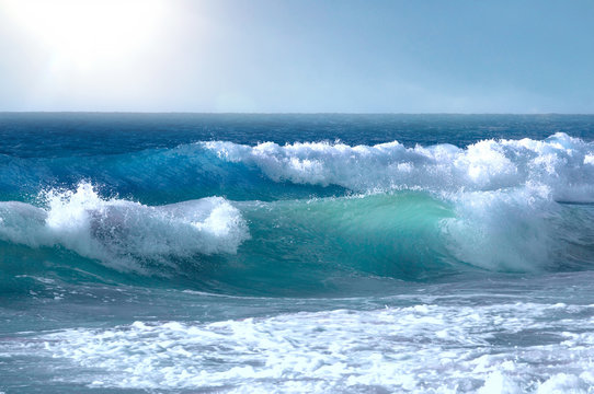 Fototapeta Beautiful big waves of the ocean or the sea in the summer bright blue, azure and turquoise colors in the early morning in sun light on a pure blue sky. Beautiful combs white sea foam.