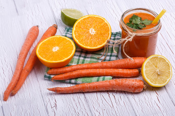 orange detox coctail with oranges and carrots lies on white tabl