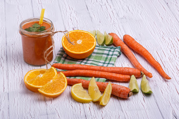 orange detox coctail with oranges and carrots lies on white tabl