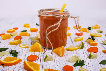 orange smoothie stands on white table with many small pieces of