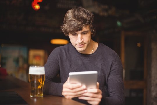 Man with glass of beer using digital tablet in counter