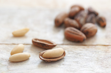 Some peeled pine nuts next some out shelds on a white wooden table.