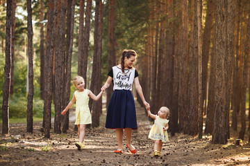 Naklejka na ściany i meble Mother and two little daughters walking in the forest. Family en