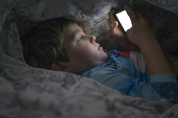 Young boy playing with cell phone under duvet © stockedup