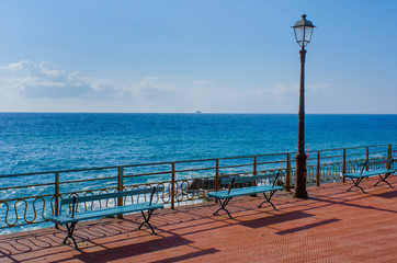 two benches and an old lantern on the walking promenade of Nervi, Genoa, in Italy with a wonderful view to the Mediterranean Sea on a sunny day with a boat visible far away on the horizon