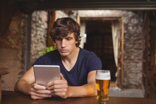 Man using digital tablet with beer glass on table