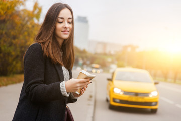 Brunette with phone on background of passing yellow taxi