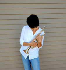 Female trumpet player holding her horn outside.