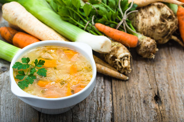 Vegetable soup in a bowl and fresh vegetables on wooden table