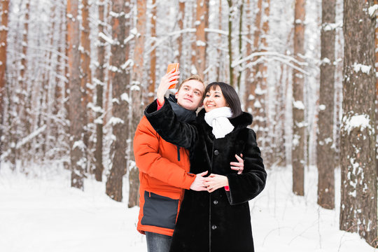 people, season, love, technology and leisure concept - happy couple taking photo with smartphone on over winter background