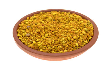 Bowl of bee pollen granules on a white background side view.