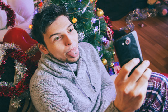 Hombre joven tomándose una foto con su teléfono móvil en su casa en navidad 
