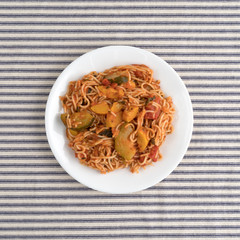 Angel hair pasta with zucchini and spinach on a plate atop a striped table cloth.