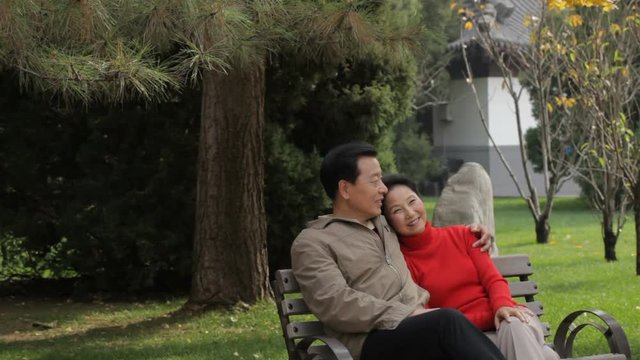 MS Elderly couple sitting and embracing on park bench / China