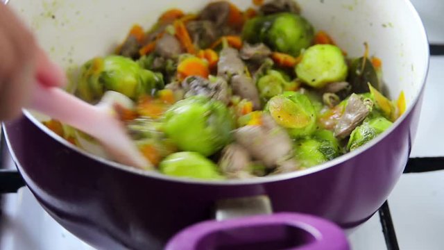 Process of cooking chicken hearts with Brussels sprouts- open cover mixing the ingredients in a pan and cover closing