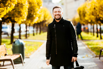 Fototapeta premium handsome and young man in a black coat standing in the park
